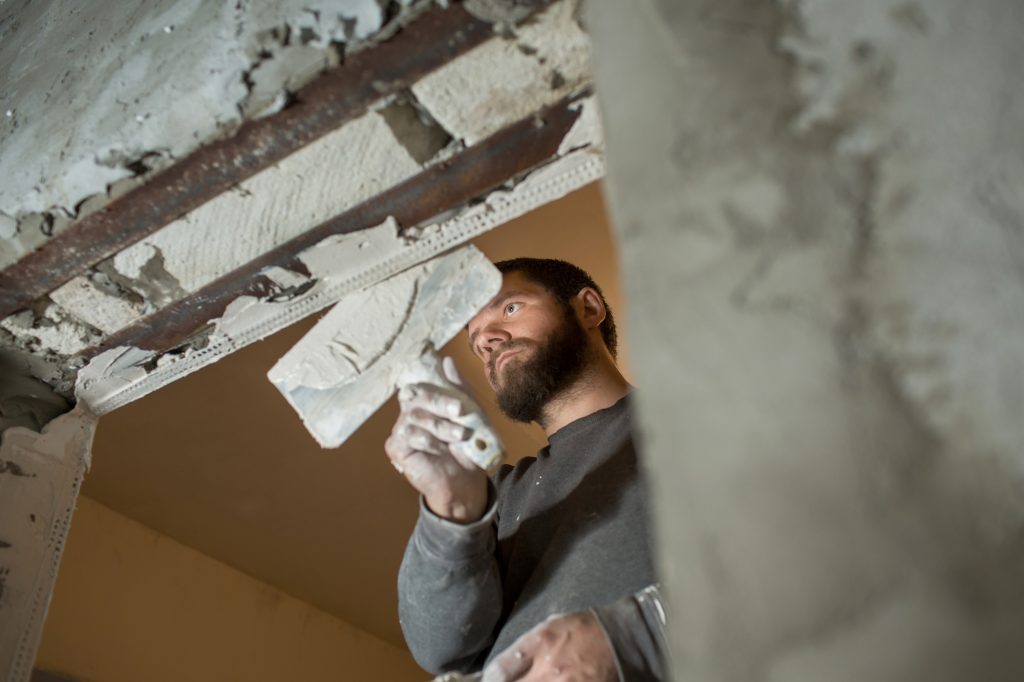 a male plasterer plasters a concrete wall with a spatula.