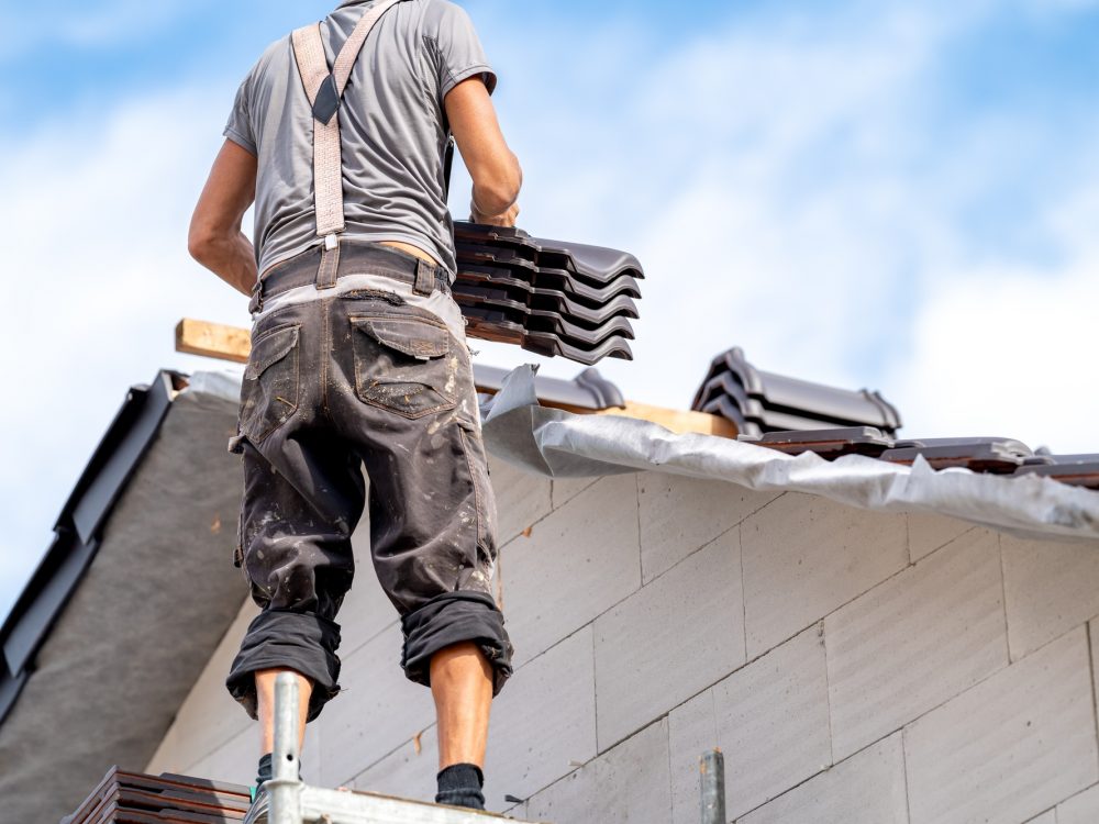 a builder on scaffolding is building the roof of a house from ceramic tiles a builder on scaffolding is building the roof of a house from ceramic tiles